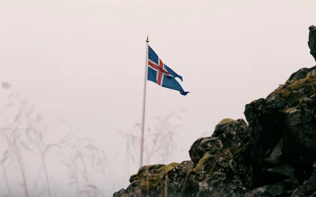 Iceland flag flying on top of a rocky cliff.