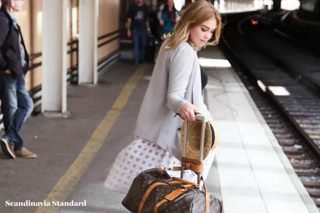 A woman with a louis vuitton bag on a train platform.