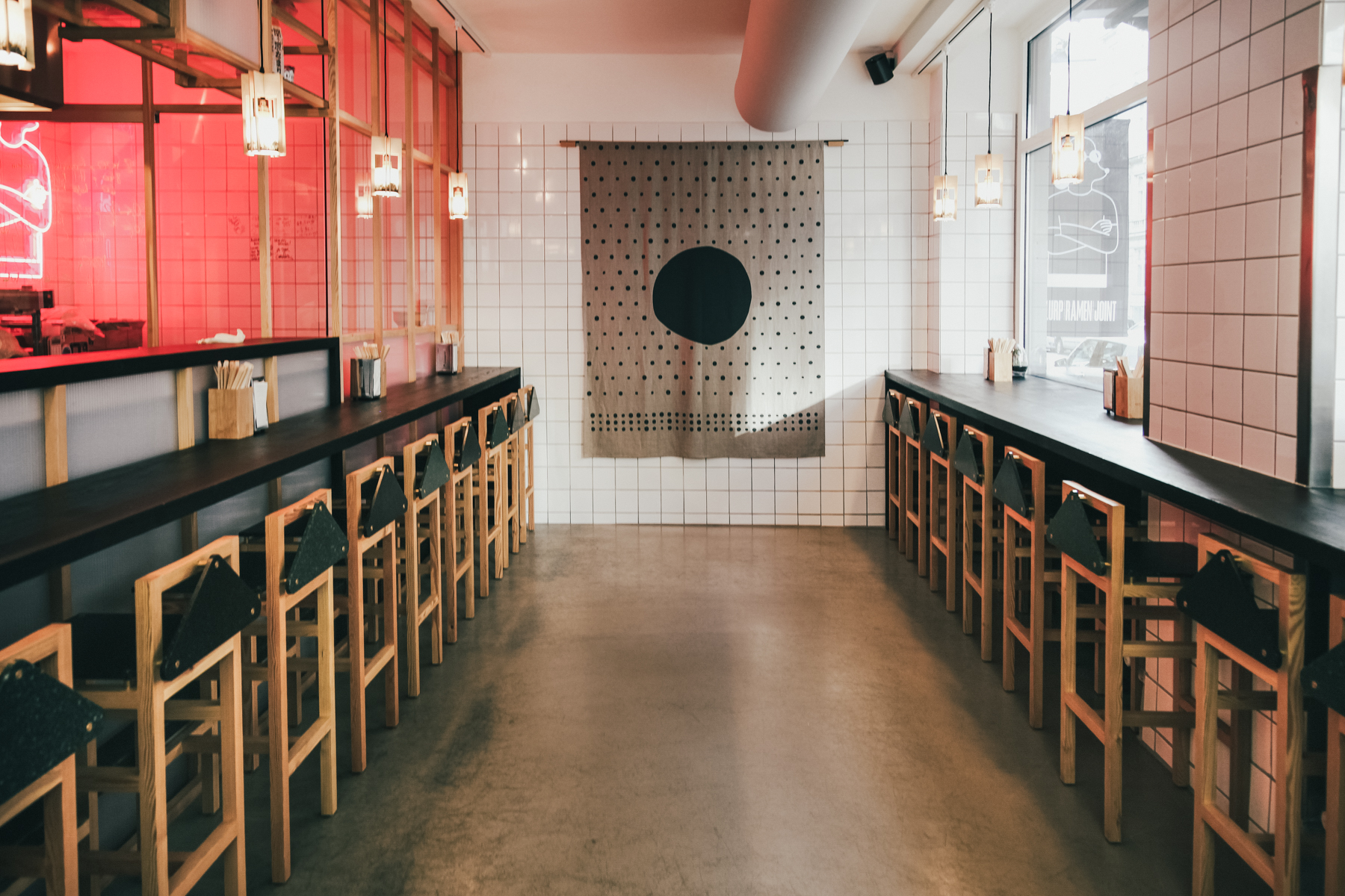 A long bar in a restaurant with stools and red lights.