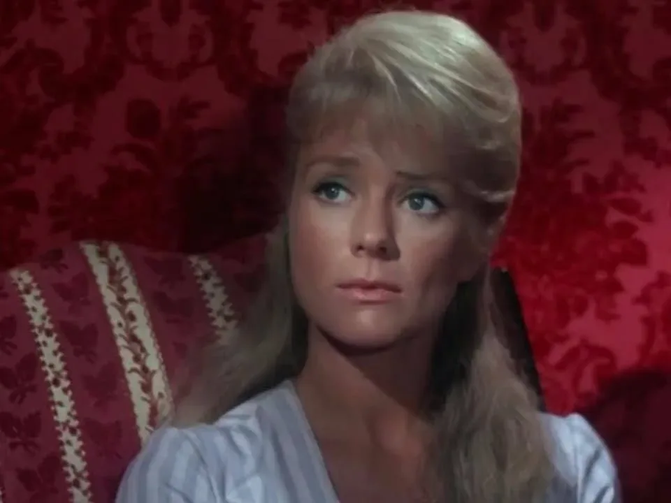 A woman, possibly resembling Inger Stevens, is sitting in a red chair.