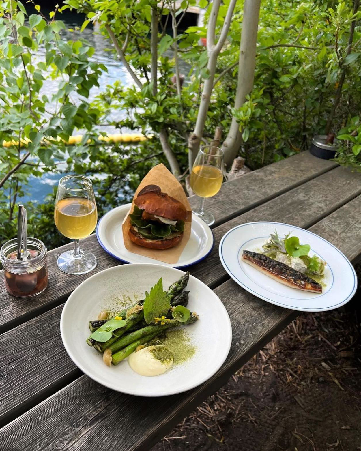 Three plates of food on a wooden table next to a river in Copenhagen.