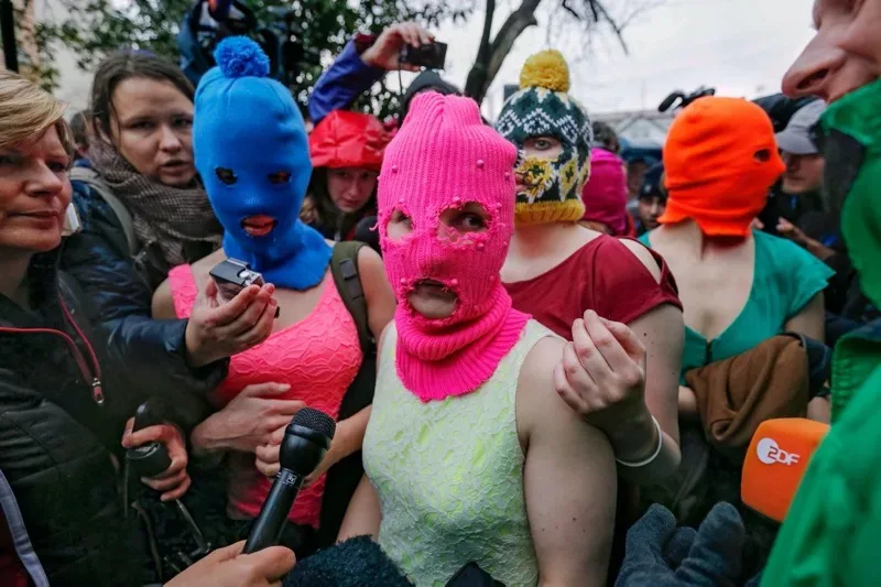 A group of people wearing colorful masks in front of a group of reporters.