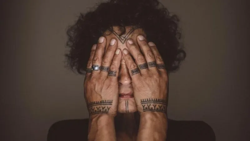 A woman with tattoos covering her face with her hands.